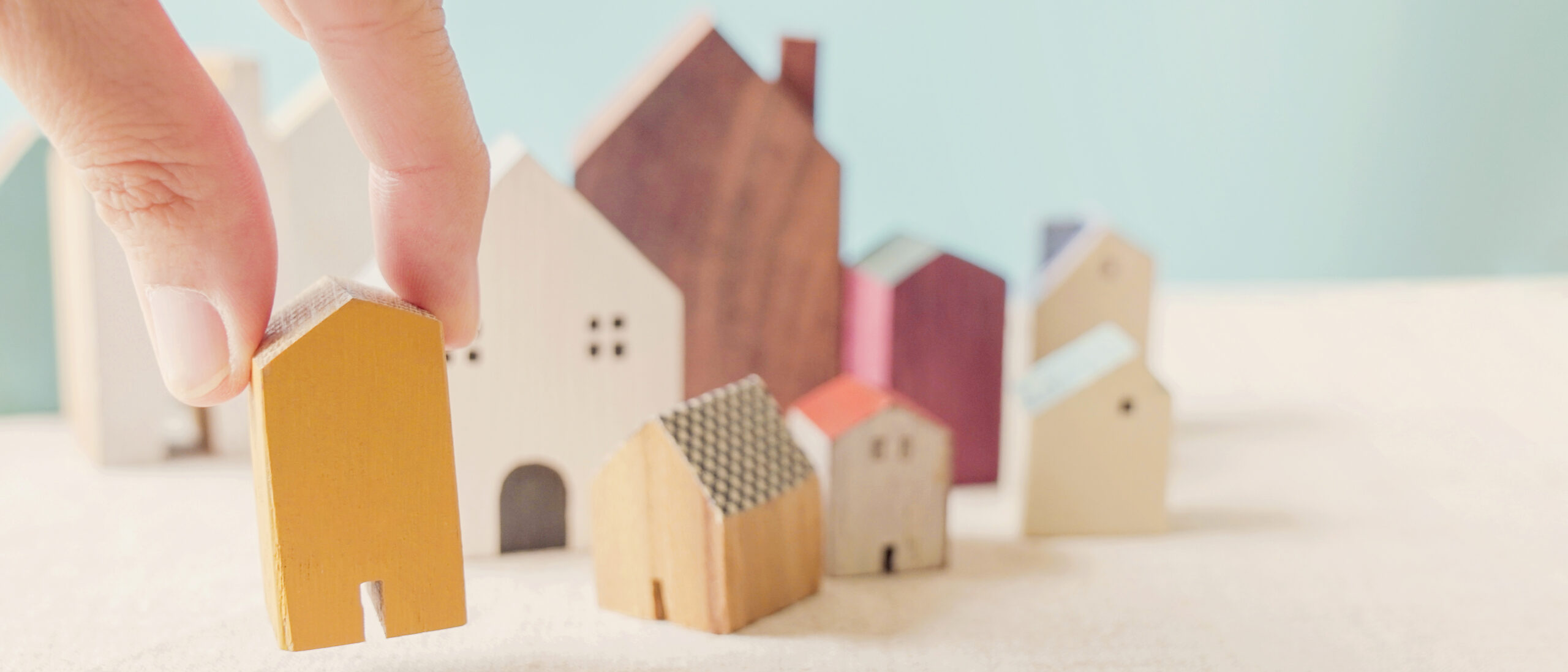 Hand choosing yellow miniature house, searching perfect property